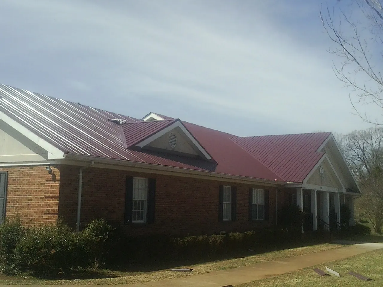 Red metal roof with gabled entries on a long brick building, from a Hail Damage Roof Repair job in Santa Ana