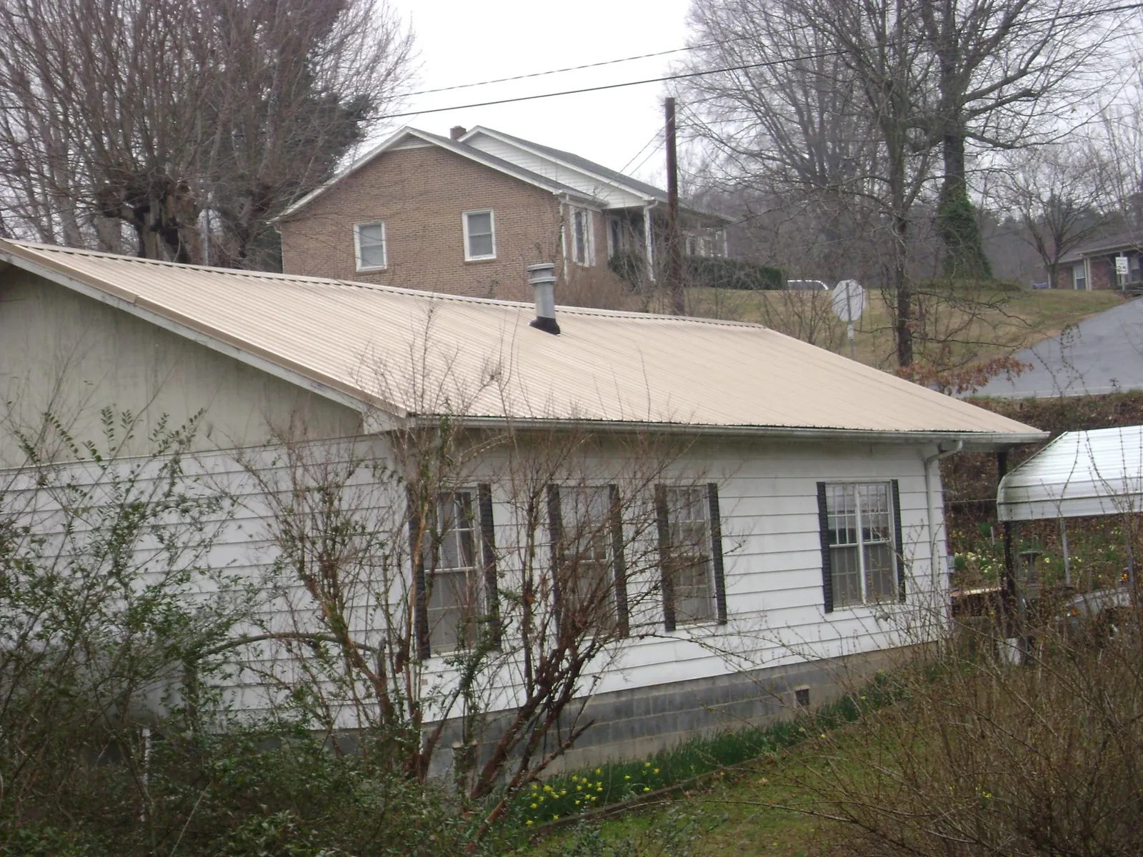 Tan metal roof on a white sided house set into a hillside — Commercial Roofing by Roofing Brothers in Santa Ana